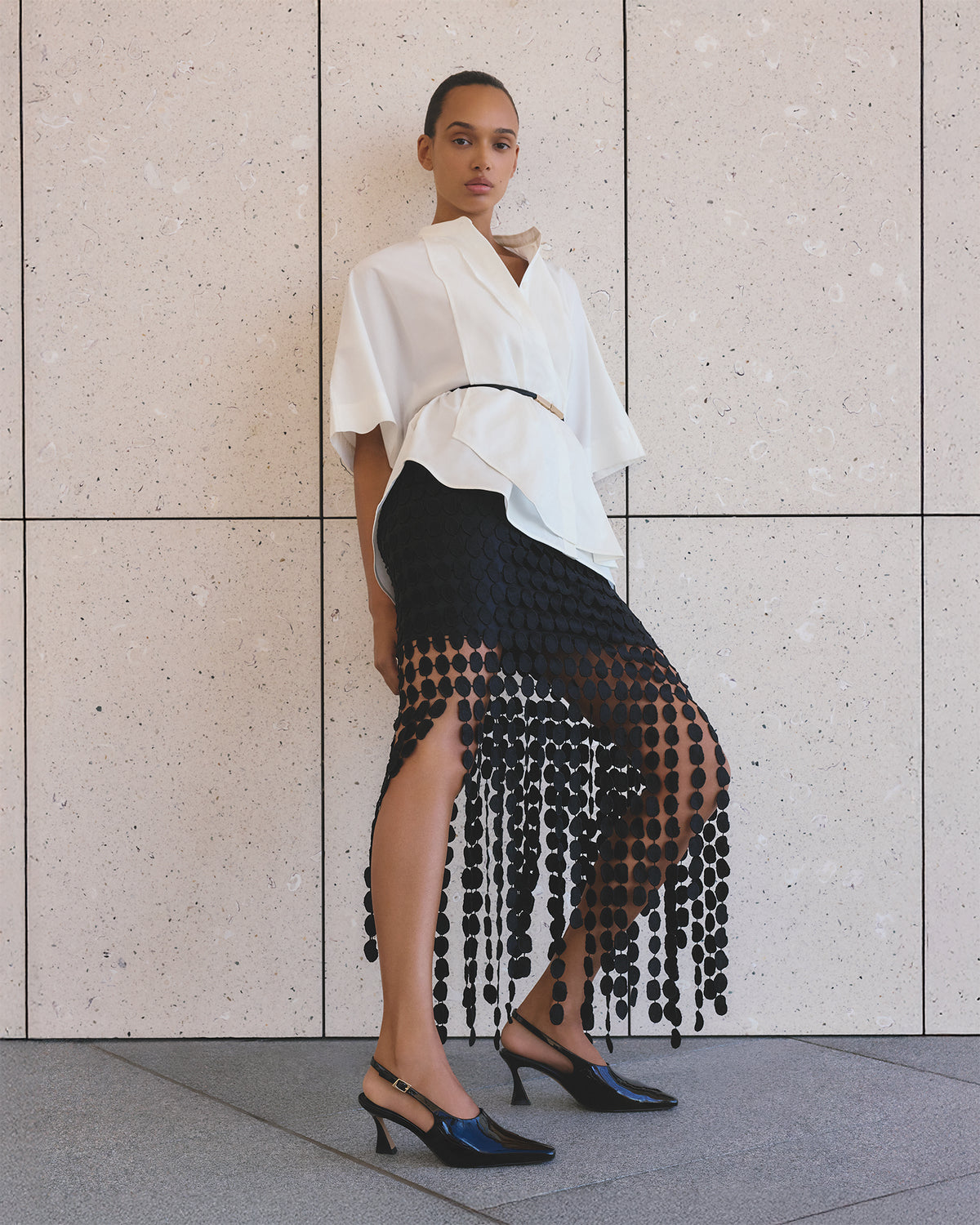 Woman wearing a white top and black sheer skirt against a tiled wall.