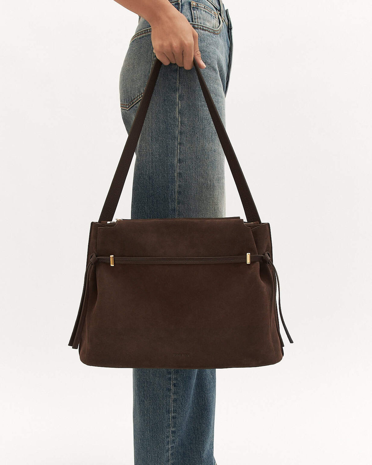 Brown leather handbag held by a person wearing blue jeans on a white background