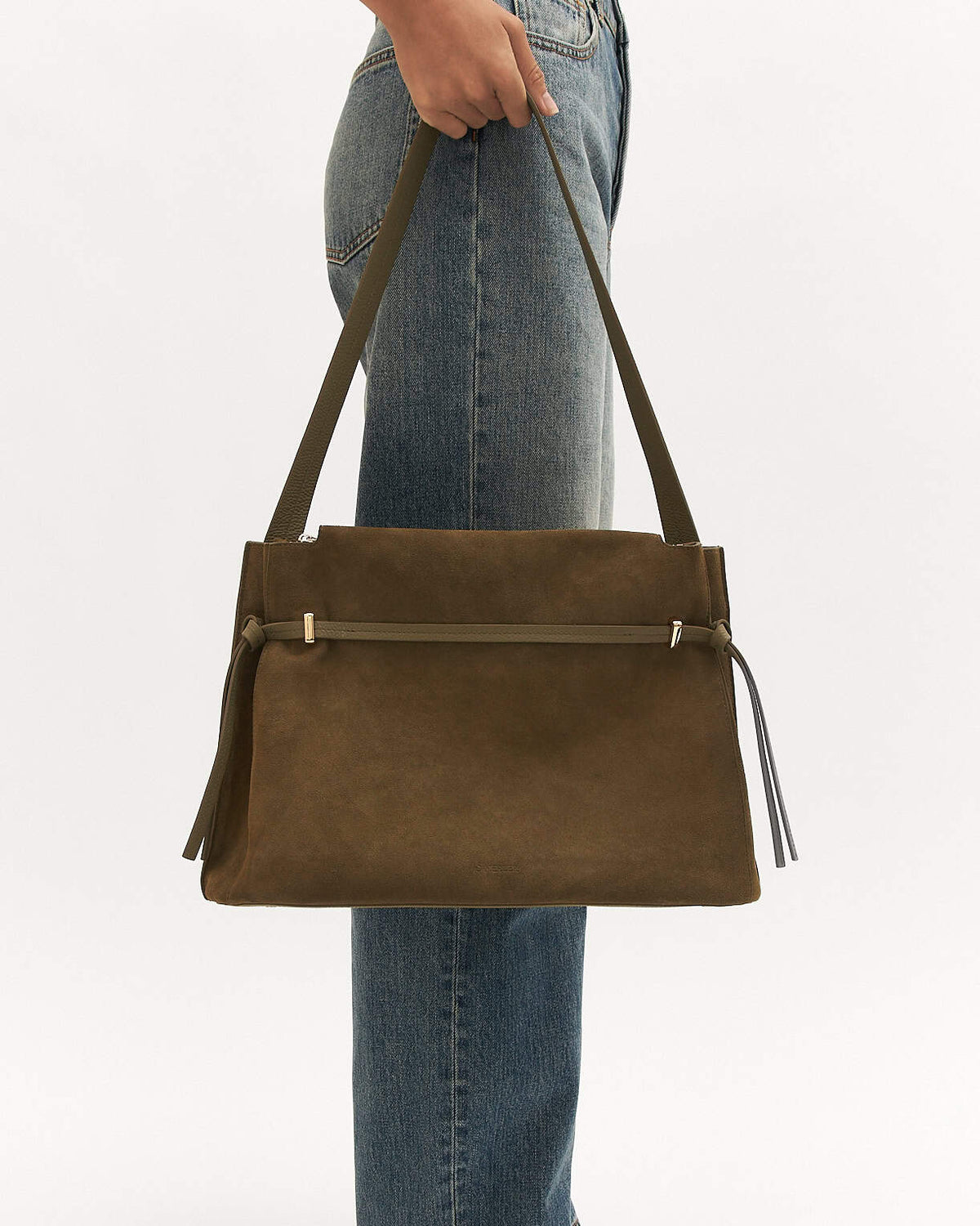 Brown leather handbag held by a person wearing blue jeans on a light gray background
