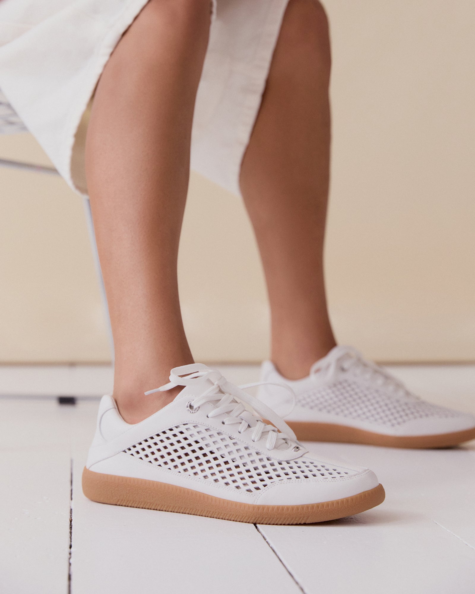 White sneaker with a brown sole on a light gray background