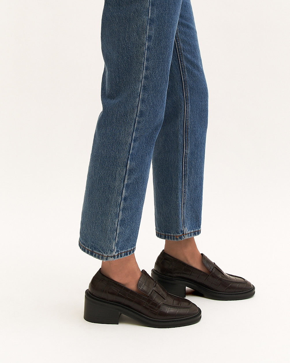 Person wearing blue jeans and brown loafers on a white background