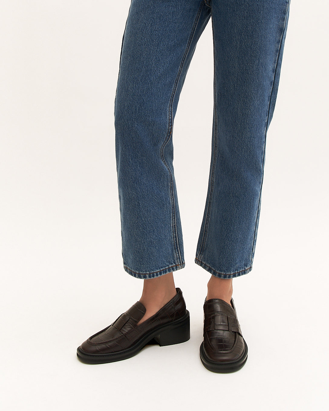 Person wearing blue jeans and brown loafers on a white background
