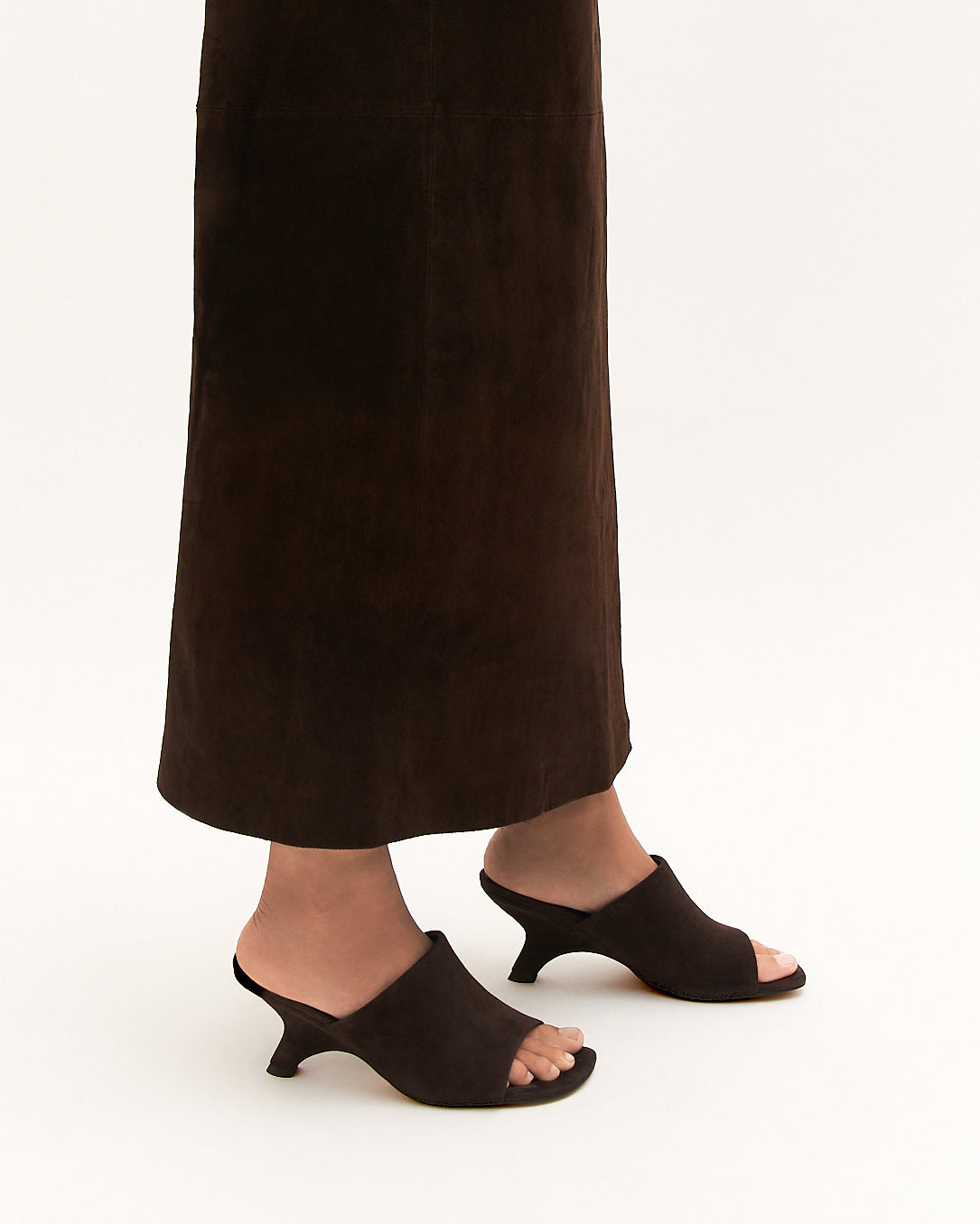 Person wearing black open-toe high-heeled shoes and dark pants on a white background