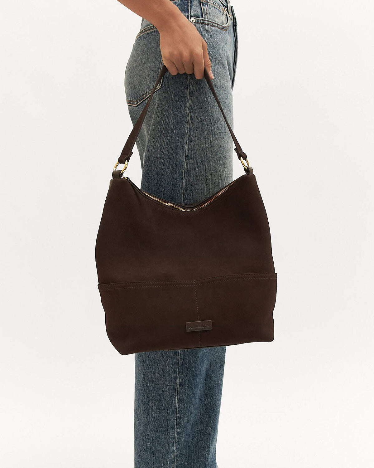 Brown handbag held by a person wearing blue jeans on a white background