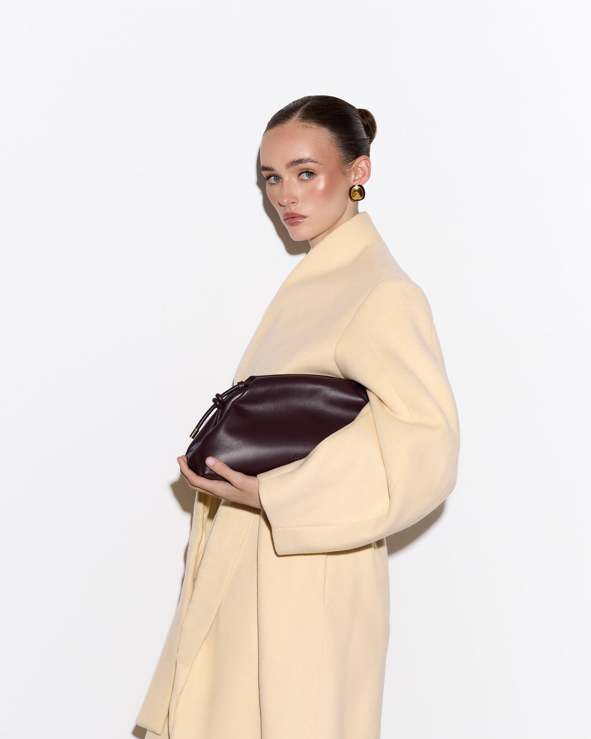Woman holding a brown leather bag wearing a beige coat on a white background