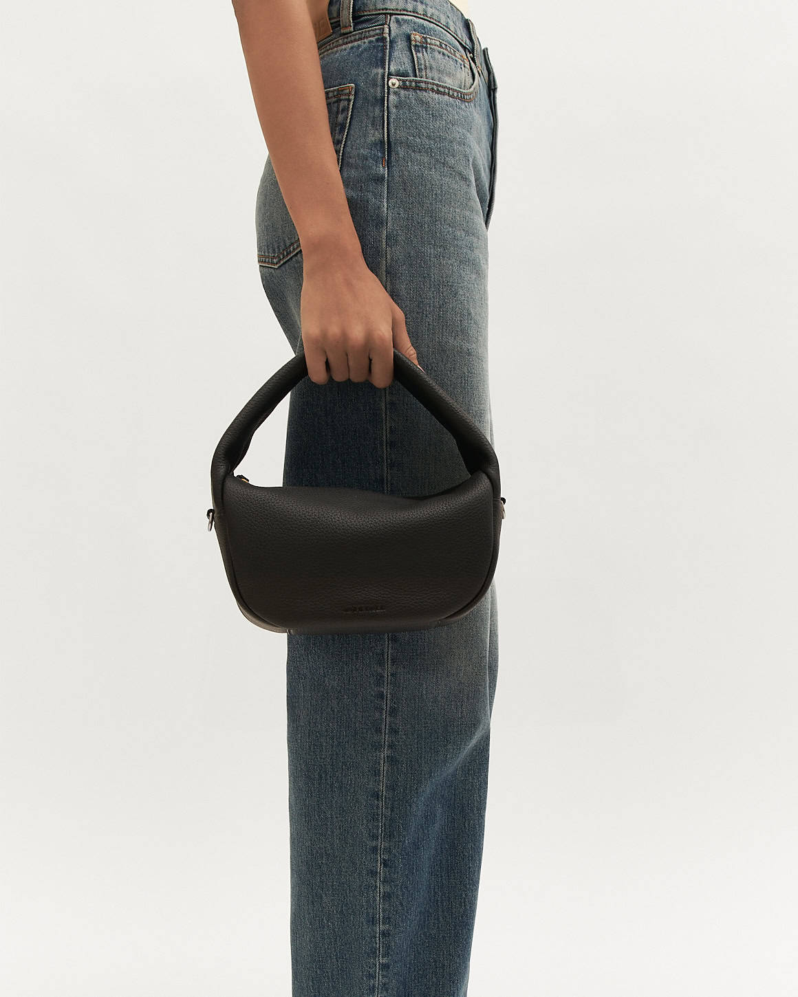 Person holding a black handbag with blue jeans on a white background