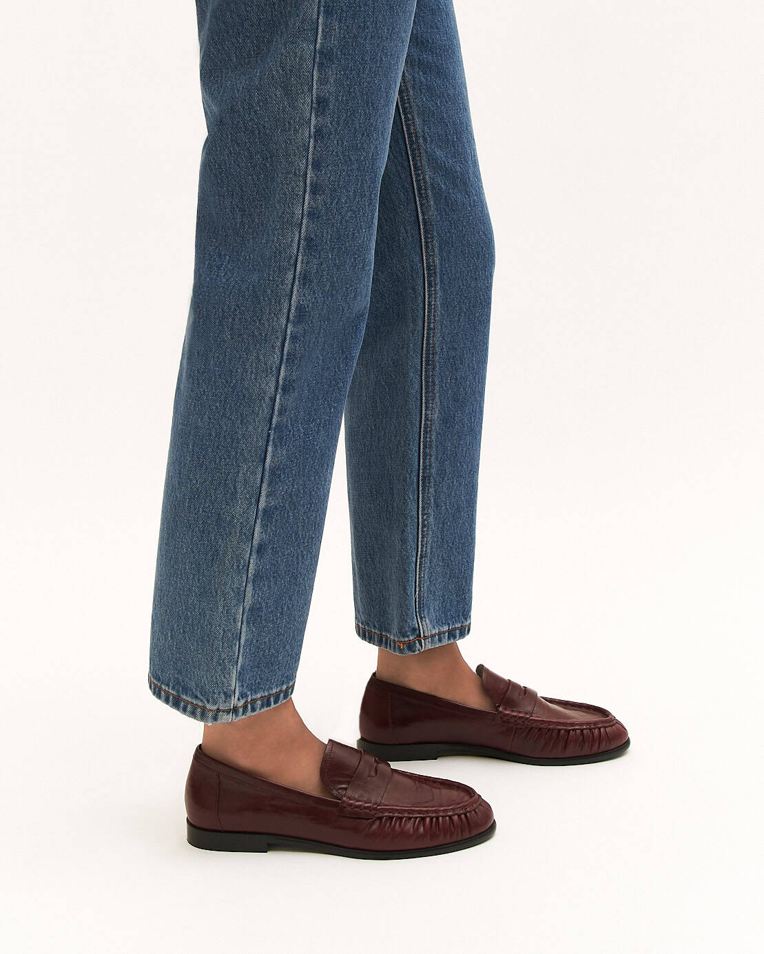 Brown loafers worn with blue jeans on a white background