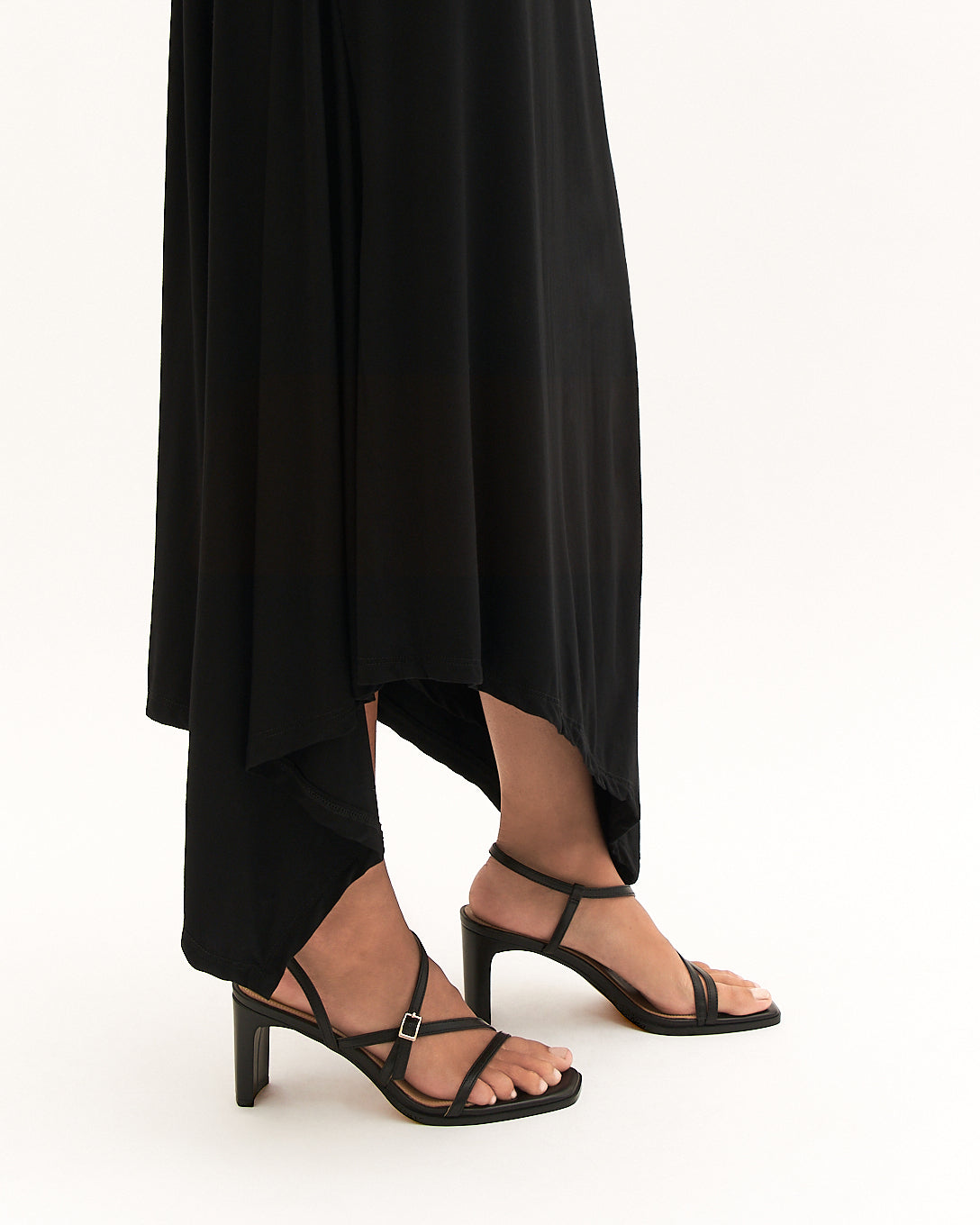 Black high-heeled sandals worn with a long black dress on a white background