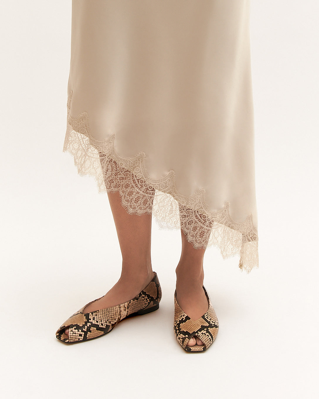 Person wearing snake print flats with a lace-trimmed skirt on a white background
