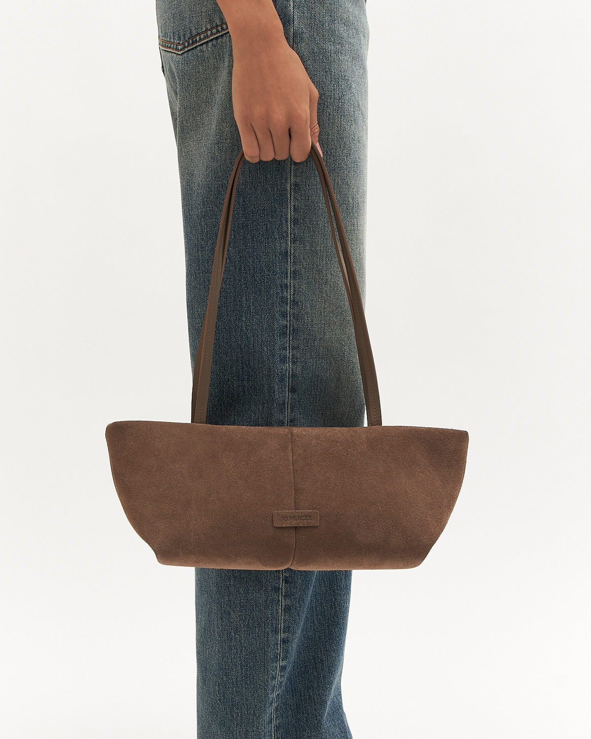 Brown suede handbag held by a person wearing blue jeans on a white background