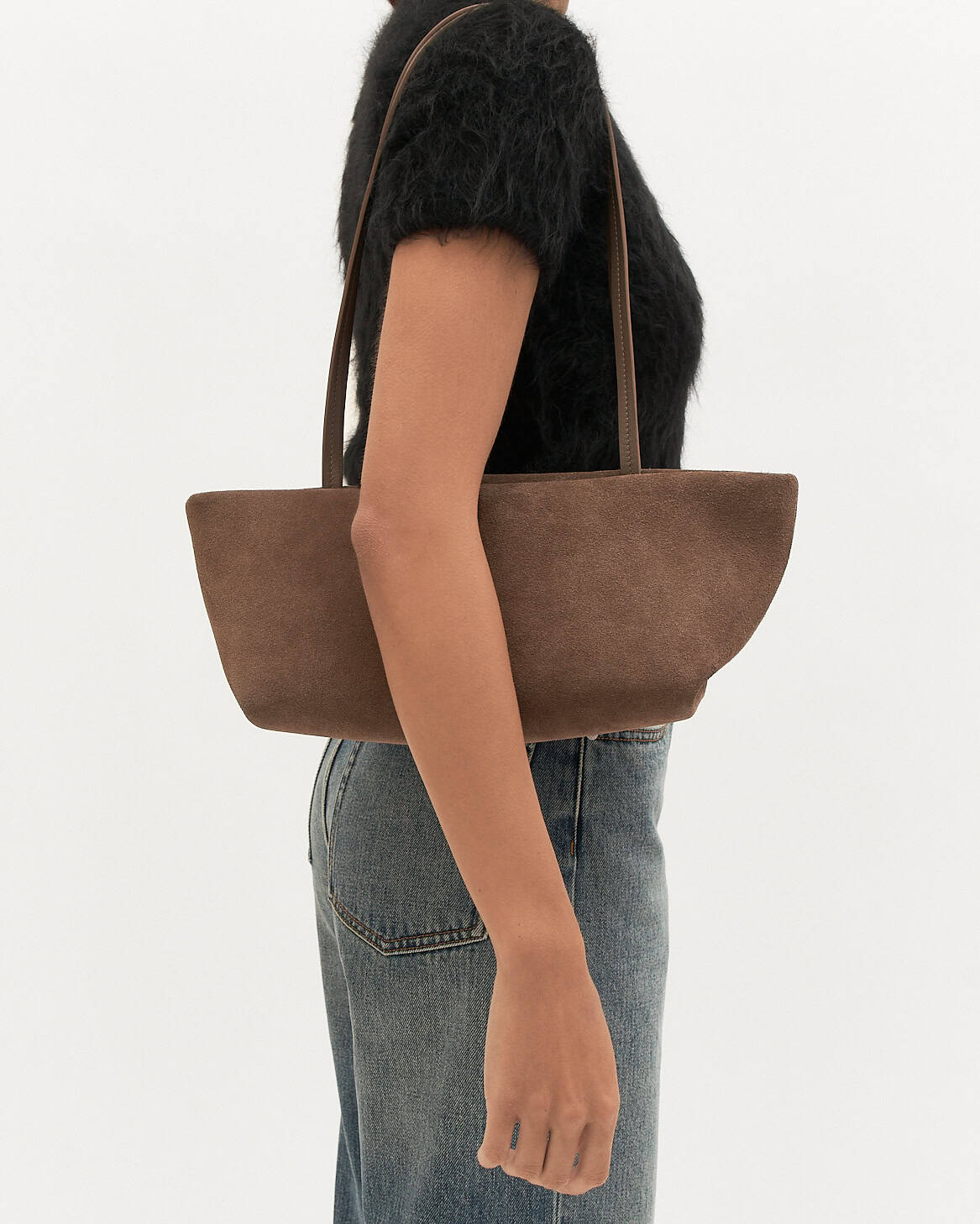 Person holding a brown suede handbag on a white background
