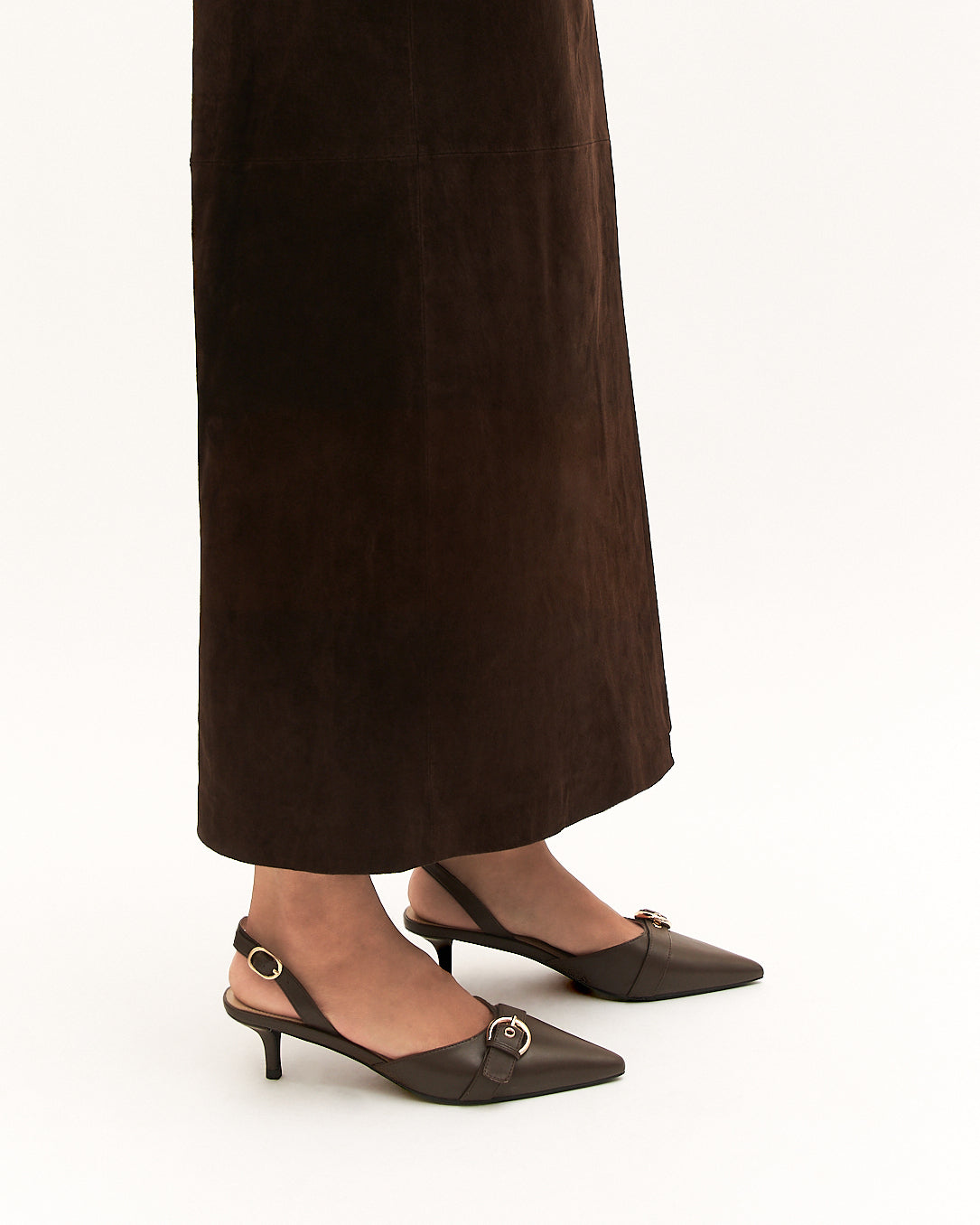 Brown high-heeled shoes worn with a long dark brown skirt on a white background