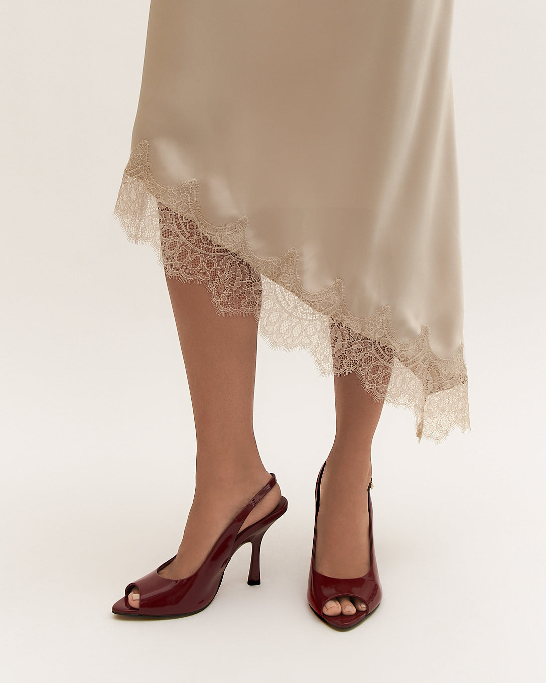 Person wearing a beige skirt with lace trim and high-heeled shoes on a white background
