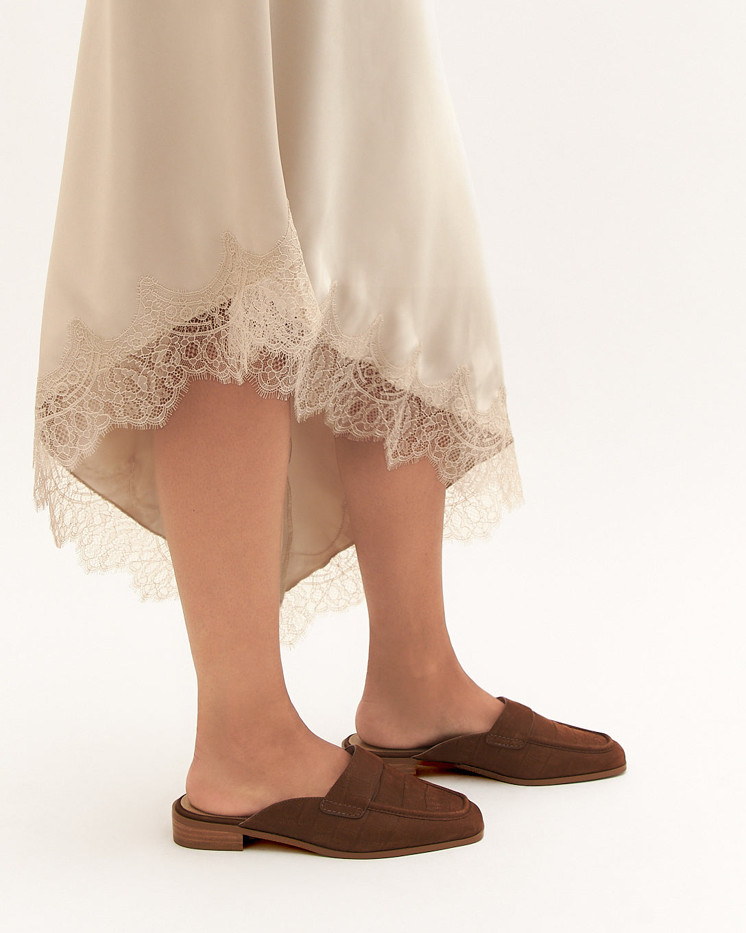 Person wearing a beige dress with lace trim and brown shoes on a white background