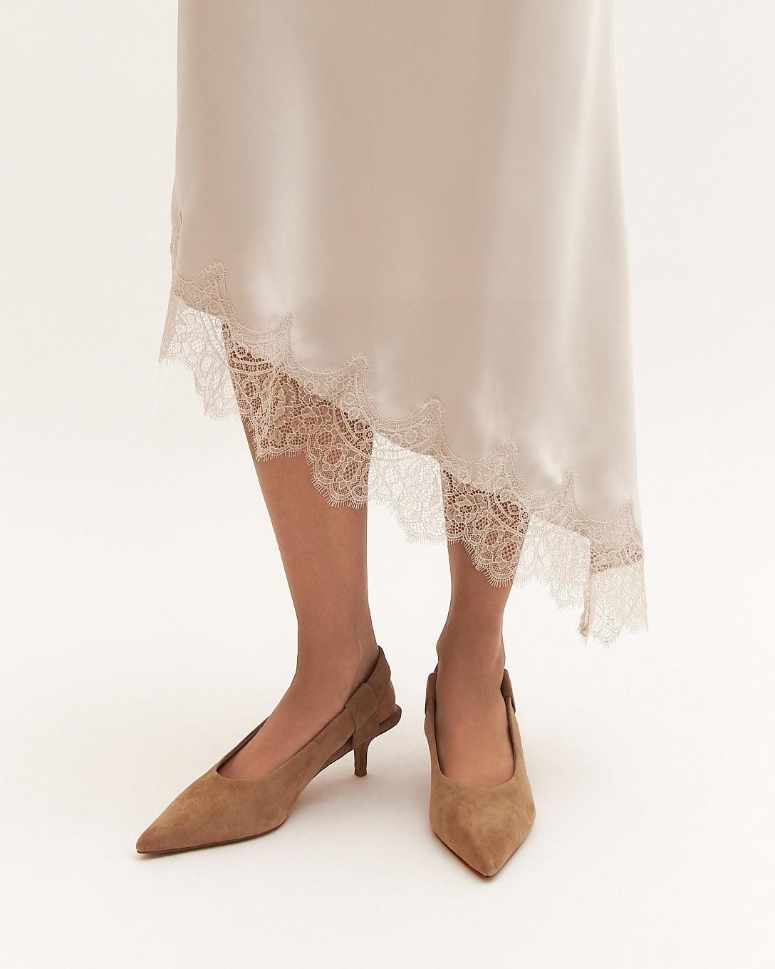 Brown suede shoes worn with a lace-trimmed dress on a white background