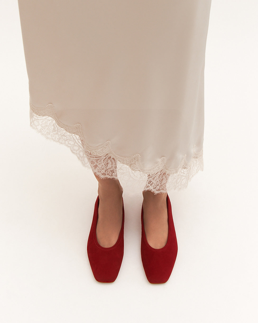 Red shoes worn with a white skirt on a light background