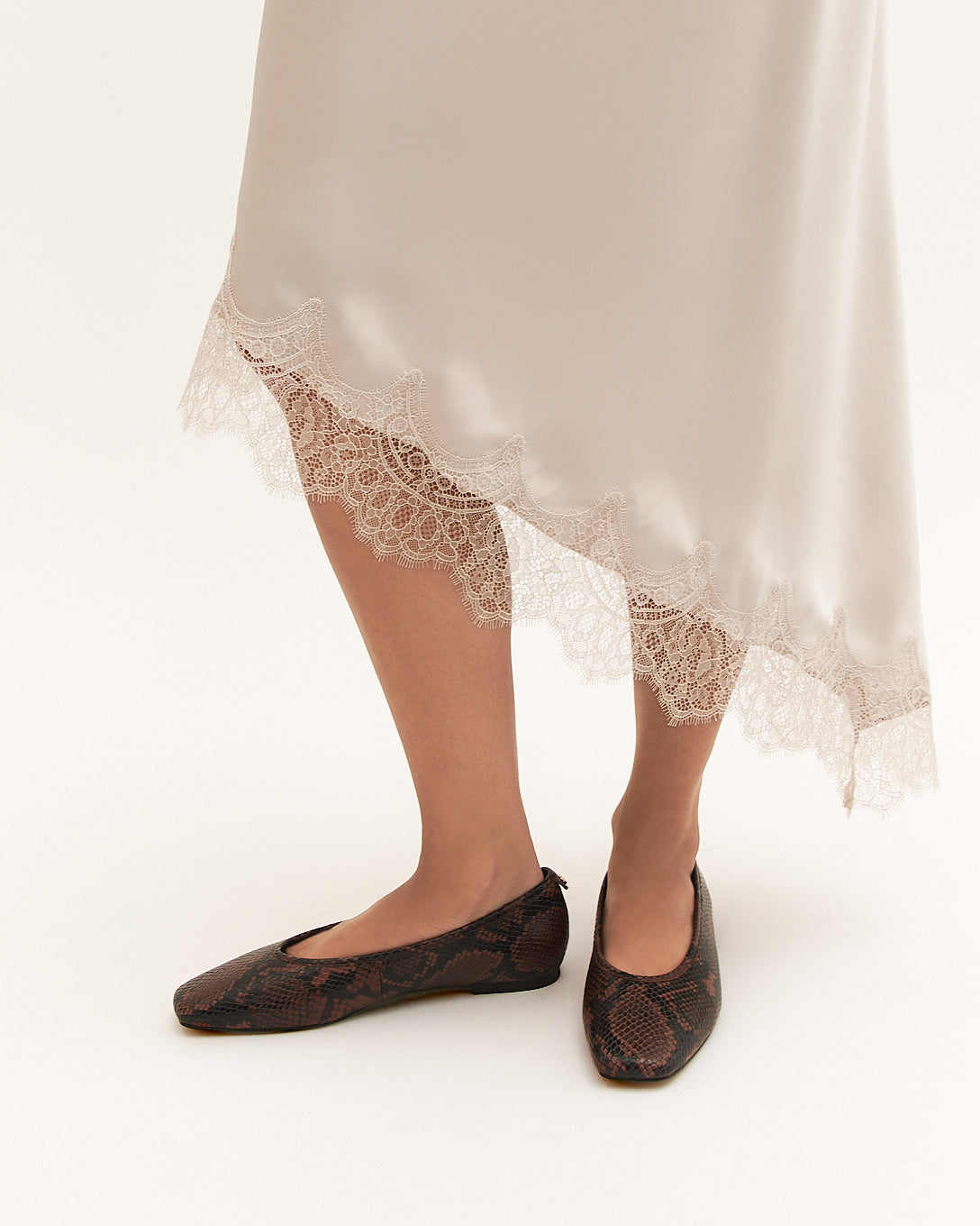 Person wearing a white lace-trimmed dress with black shoes on a white background