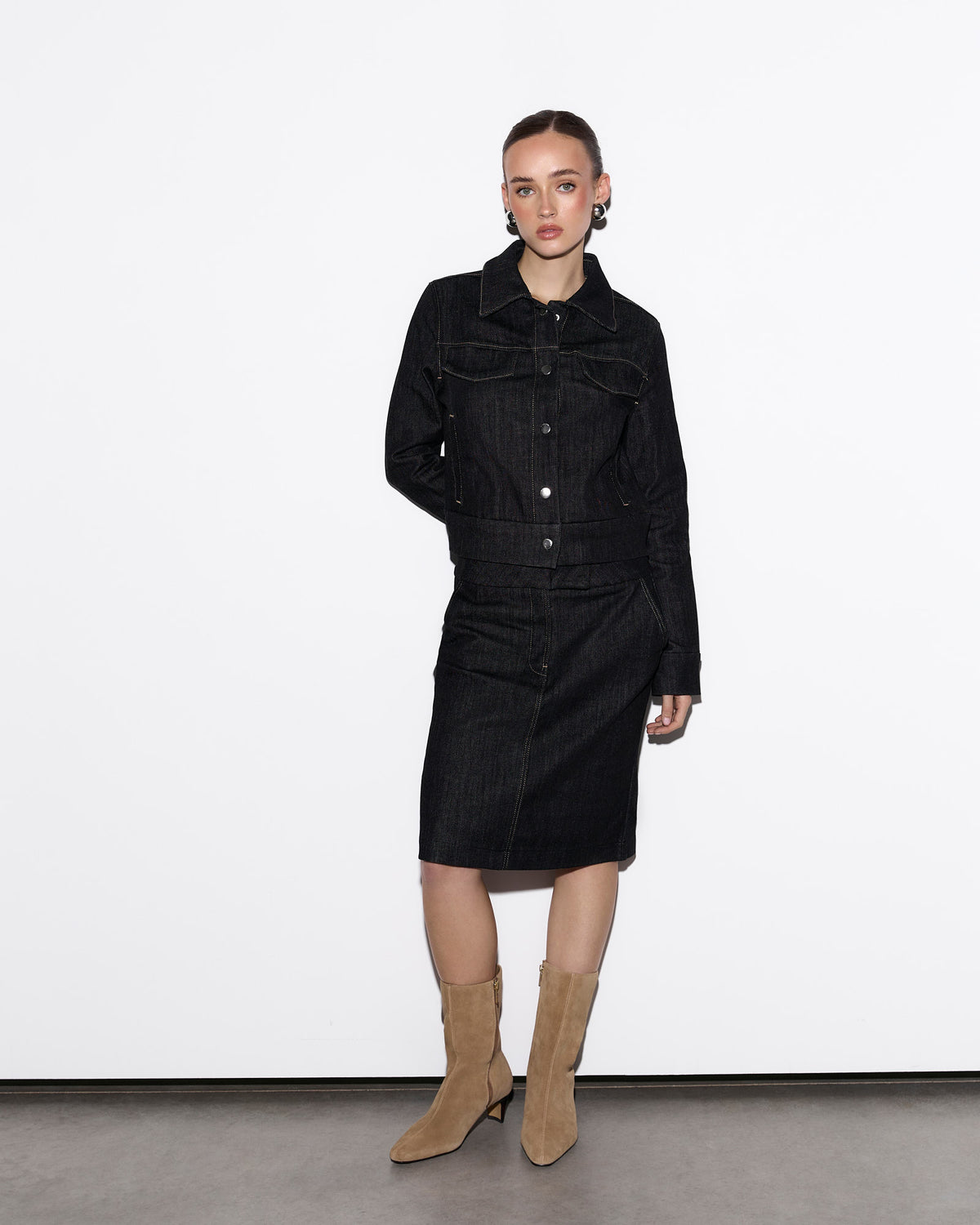 Person wearing a black denim outfit with beige boots on a white background