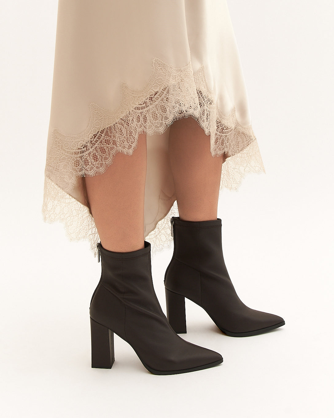 Black ankle boots worn with a beige lace-trimmed dress on a white background