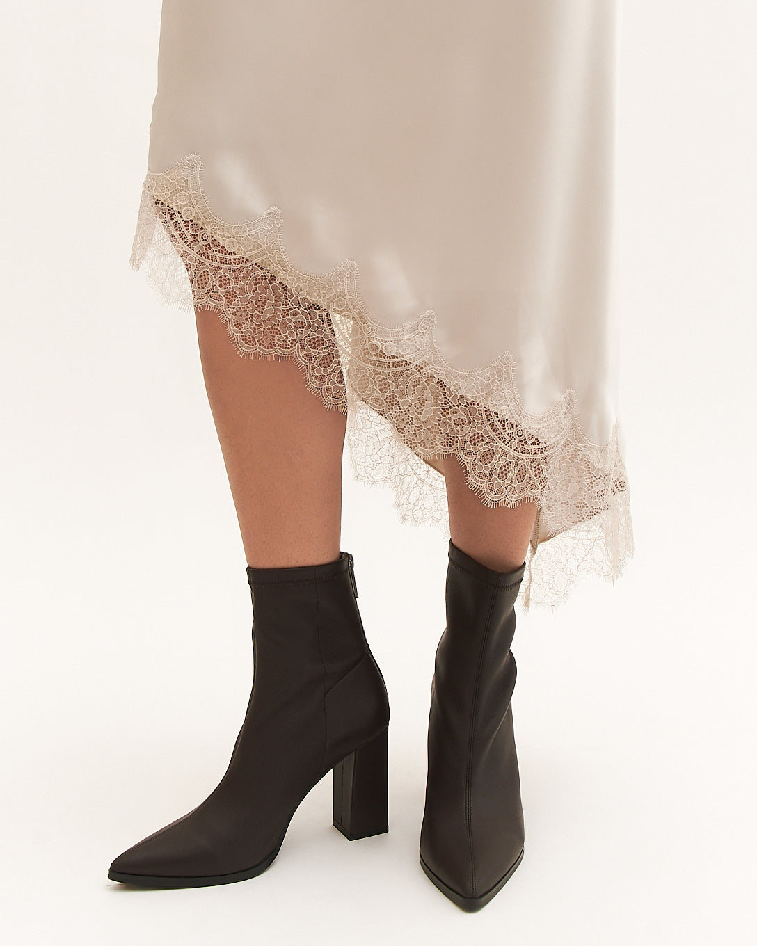 Black knee-high boots worn with a beige lace-trimmed dress on a white background