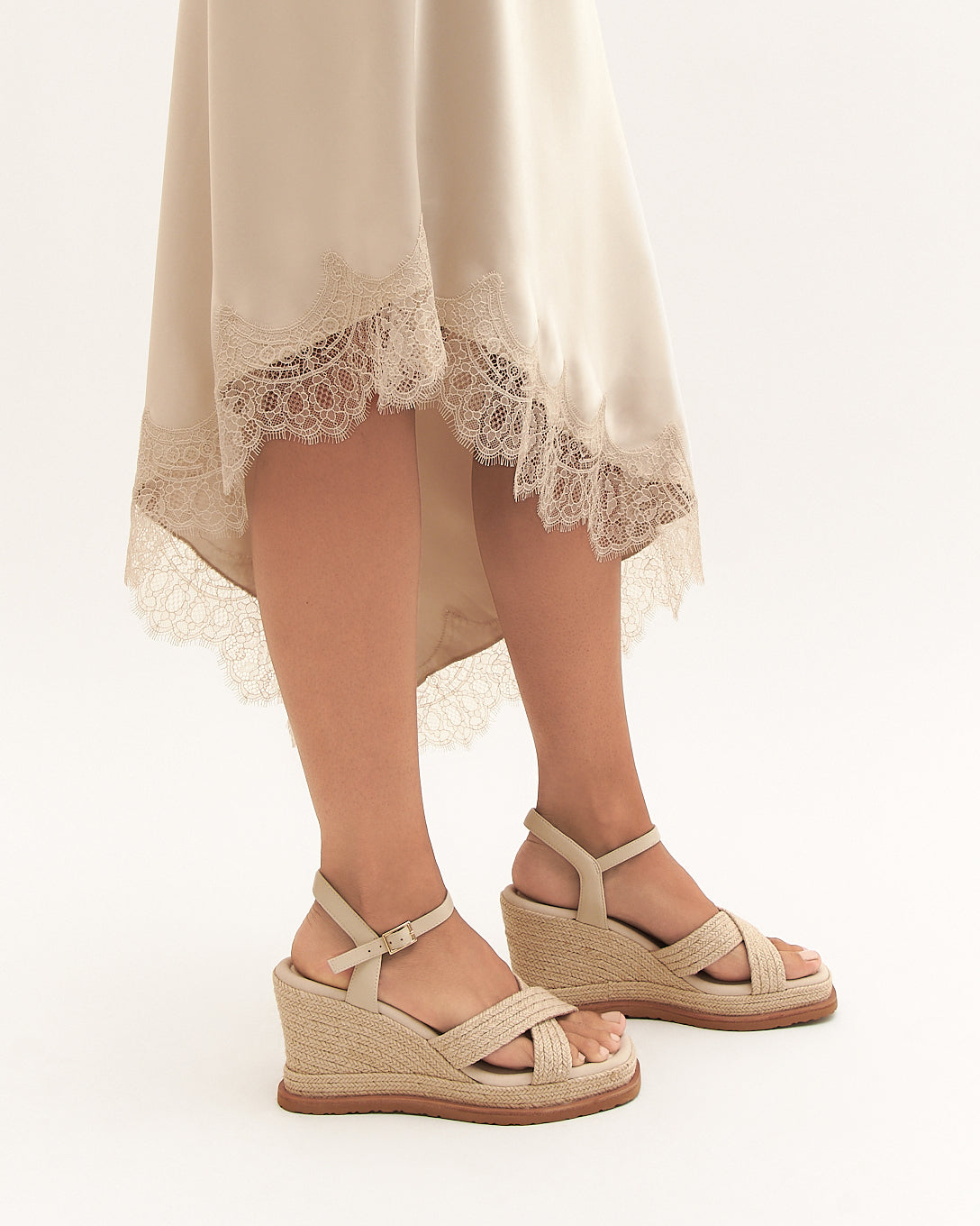Beige sandals worn with a light-colored dress on a white background