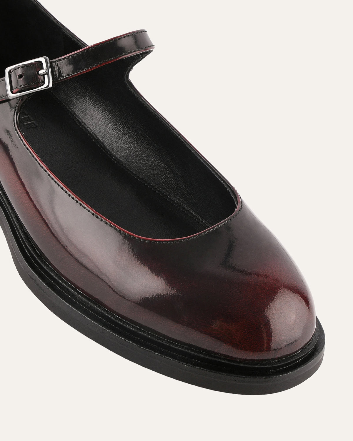 Shiny black shoe with a strap and buckle on a light gray background