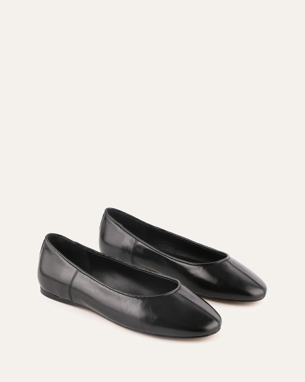 Pair of black flat shoes on a light beige background